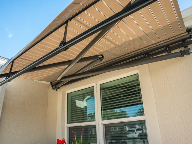 Crossarm motorized awning with bronze housing and putty regimental-stripe fabric, partially extended