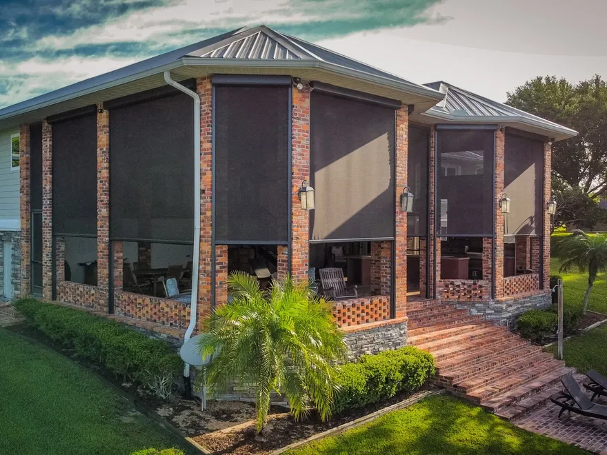Multiple motorized screens lowered across the exterior of a brick home framed by palms