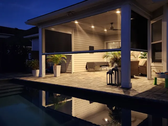 Motorized insect screens around a residential pool lit at night