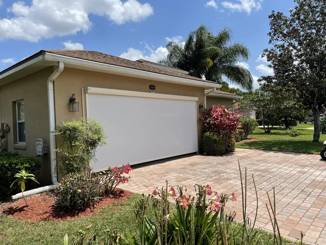 Motorized garage screen lowered across a stucco-home garage opening