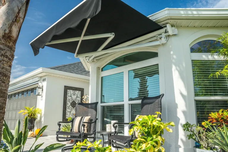 Motorized retractable awning with white housing and black scalloped fabric partially extended over a residential patio