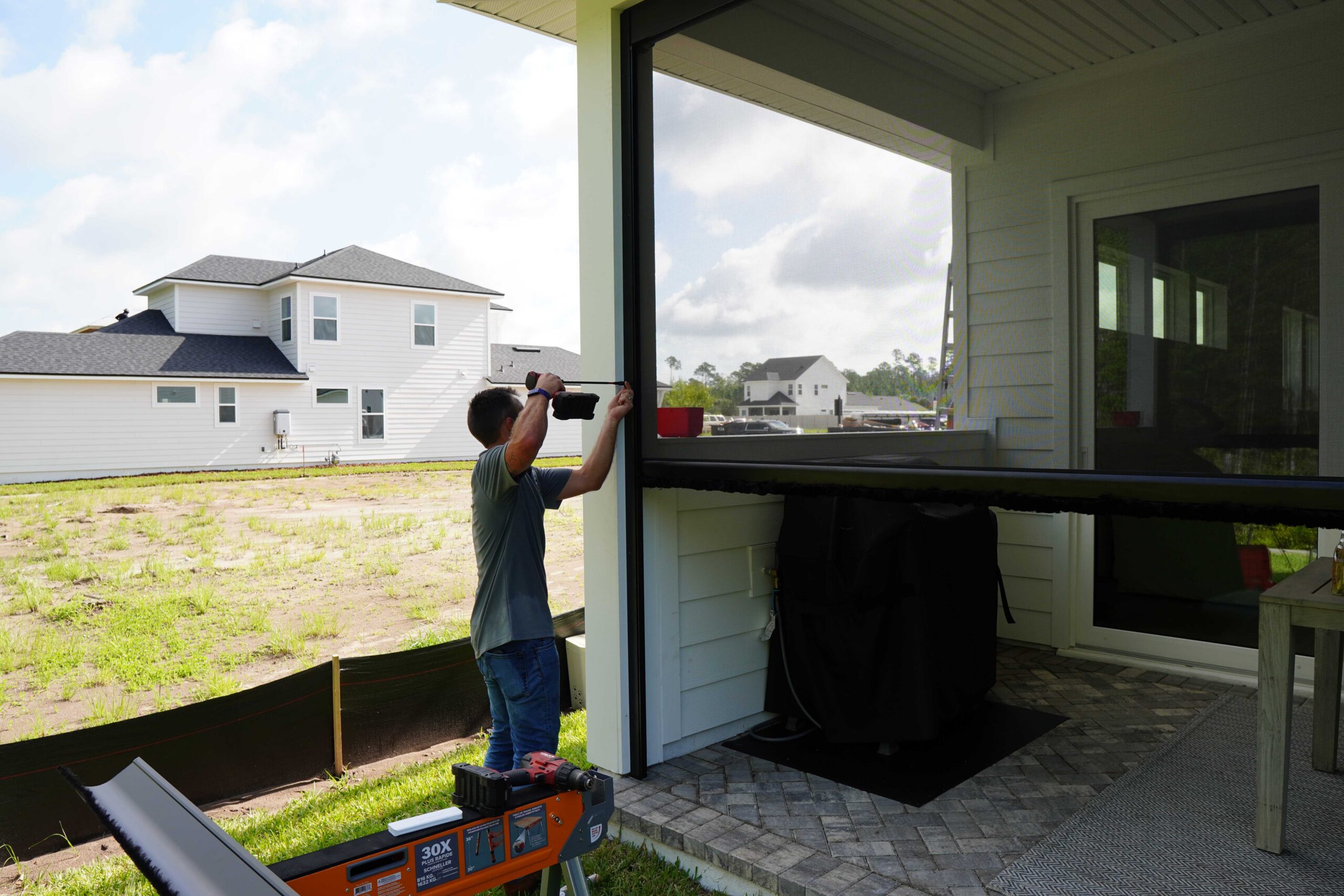 Cheetah Screens installer mounting a retractable screen track on a covered patio